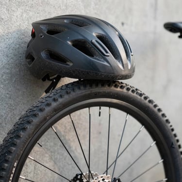 Close-up of a bicycle tyre and helmet resting against a concrete wall, natural outdoor daylight, focus on material detail