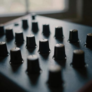 Extreme close-up of vintage analog synthesizer knobs in low-key shadow, natural window light, 35mm film