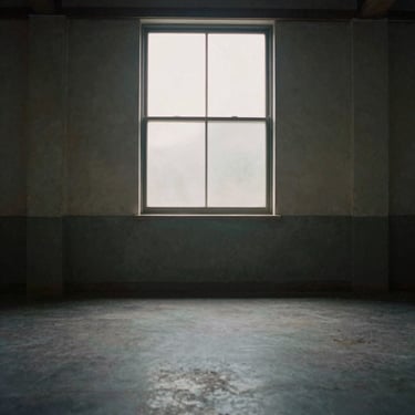 Empty rustic recording space with soft light filtering through a high window, dusty air, desaturated tones