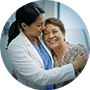 A compassionate female doctor in a white coat hugging a smiling senior patient in a medical setting.