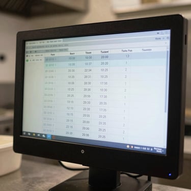 Close-up of a digital kitchen expediter screen displaying ticket times and station throughput metrics, cool bright lighting, high-contrast display