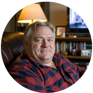 A middle-aged man in a red plaid shirt sitting in a leather chair in a cozy home library.