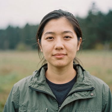 Candid close-up portrait of a female community organizer in a green jacket, soft overcast daylight, natural Pacific Northwest background, warm documentary style, 35mm film grain
