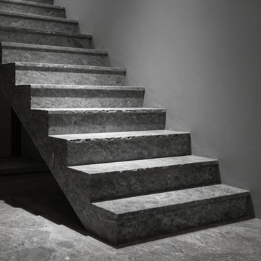 Polished slate gray stone staircase in a minimalist residence, side-lit, highlighting the precise bisotado finish.