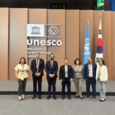 Delegates standing at the UNESCO 48th session of the World Heritage Committee with international flags.