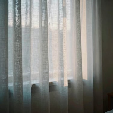 A peaceful home birthing room with soft-focus linen curtains, warm morning light filtering through a window