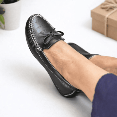 Mocasines cómodos de cuero negro para mujer con costuras blancas y un lazo decorativo.