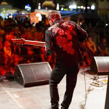Jozef Bobula in a red floral shirt playing bass on stage under warm lights before an enthusiastic crowd.