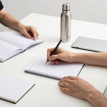 Hands arranging premium custom merchandise items like notebooks and steel bottles on a clean white desk