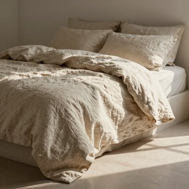 Tactile natural linen bedding crumpled gently on a low platform bed, warm morning sun casting soft shadows.