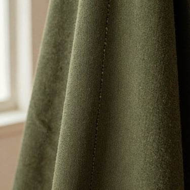 Macro texture shot of thick olive green cotton fabric showing the dense weave and single-needle stitching details, warm side light