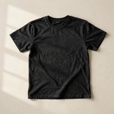 A well-worn black organic cotton T-shirt laid flat on a neutral cream surface, showing a perfectly tight, un-stretched ribbed collar under soft natural window light