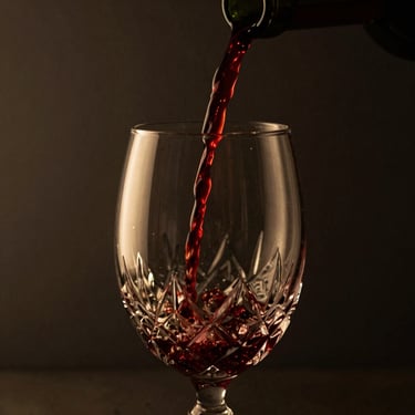 Moody close-up of red wine pouring into a crystal glass, dark background, golden reflections