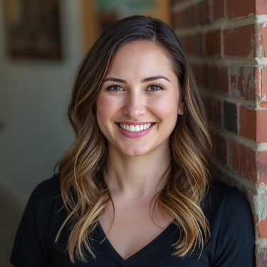Smiling woman with wavy brunette hair posing for a professional headshot against a brick wall.