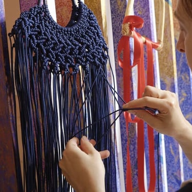 Mujer tejiendo una bolsa de macramé azul atando nudos