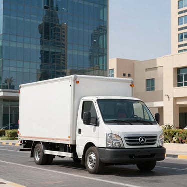 A clean white E House moving truck parked in front of modern glass office buildings in Dubai Investment Park, bright midday sun, high-contrast shadows.