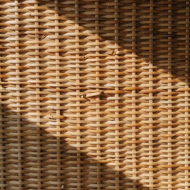 Close-up of hand-woven rattan texture catching soft morning sunlight, casting long gentle shadows, warm earth tones