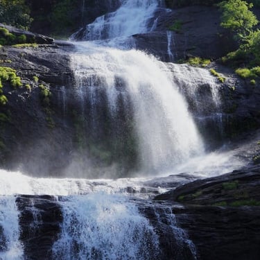 Kerala trip details - Misty Athirappilly Waterfalls cascading down rocky cliffs amidst lush tropical greenery.