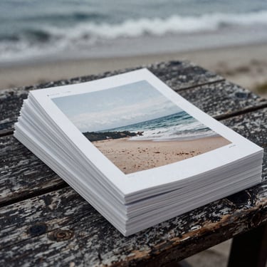 Moody film photograph of printed editorial lookbooks stacked on a weathered wooden table, overcast daylight, desaturated sea-navy tones