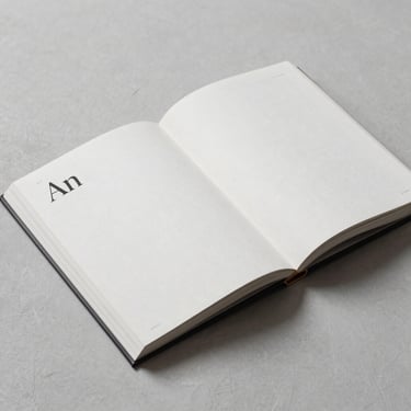 An open editorial art book on a plaster surface, displaying elegant typography and minimalist layouts under soft shadows.