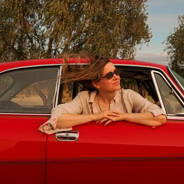 Image of a woman looking out of the passenger side window of a classic car