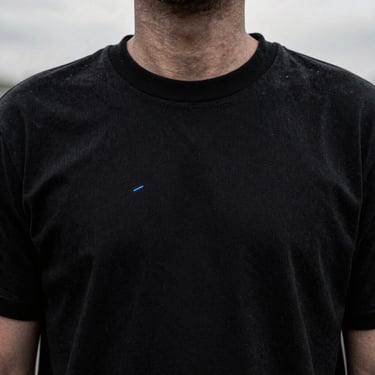 Close-up of thick collar ribs on a heavyweight black cotton tee, high-contrast desaturated lighting, 35mm lens