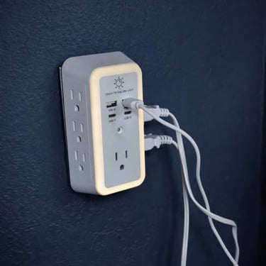 Wall-mounted outlet extender with built-in night light and USB ports charging multiple devices