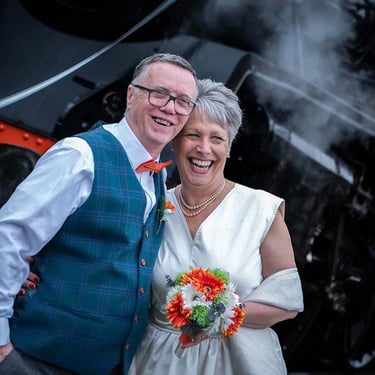 bride and groom standing in front of a steam train