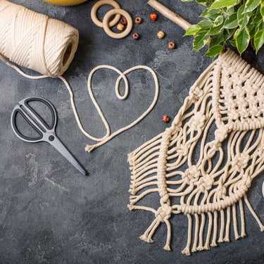 Materiales y herramientas para macramé artesanal: cordón de algodón, tijeras y pieza tejida a mano sobre una superficie.