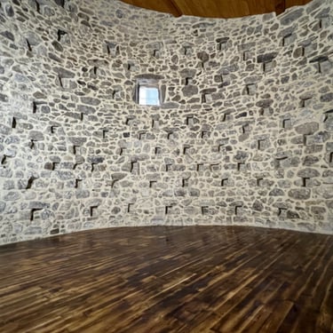 Intérieur en pierre avec mur arrondi et sol en bois.