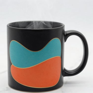 Close-up of a matte black ceramic mug with vibrant custom color print, soft steam rising, clean marble background, macro depth of field