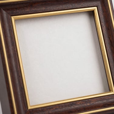 Macro shot of a premium dark wood photo frame with gold foil inlay, showcasing textured matte paper print inside, bright studio lighting