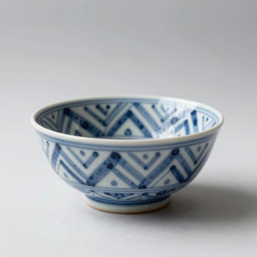 45-degree shot on white background, ceramic hand-painted decorative bowl with geometric pattern in blue and white, high-contrast studio light, no props