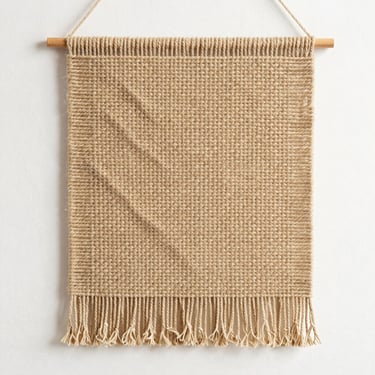 Overhead shot on white background, woven textile wall hanging in natural cotton threads, warm studio light, texture detail visible, no props