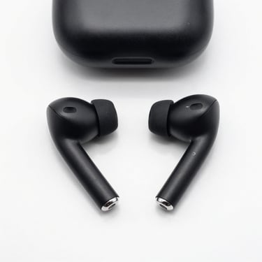 Overhead studio shot of wireless Bluetooth earbuds on a clean white surface, matte black finish, soft even lighting highlighting the charging case detail