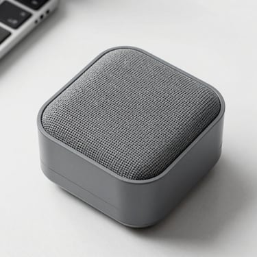 Overhead studio shot of a compact Bluetooth speaker on a white surface, fabric grille facing up, matte grey finish, clean even lighting