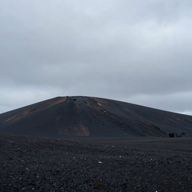 Paisaje natural austero en Islandia, colina negra volcánica bajo un cielo nublado y gris, composición minimalista y solitaria.