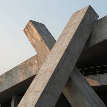Detalle arquitectónico abstracto, líneas de hormigón gris que se cruzan en un ángulo agudo, luz difusa de tarde, sin personas.