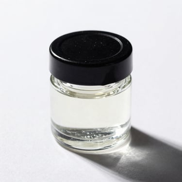 Macro studio shot of a small glass concentrate jar with a black lid, resting on a stark white background with sharp shadows.