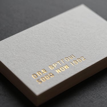 Close-up of premium textured business cards with gold foil embossing on heavy cotton paper, dramatic side lighting