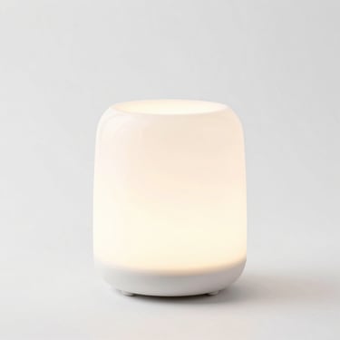 Minimalist ceramic essential oil diffuser with a soft warm glow, clean white background, studio light