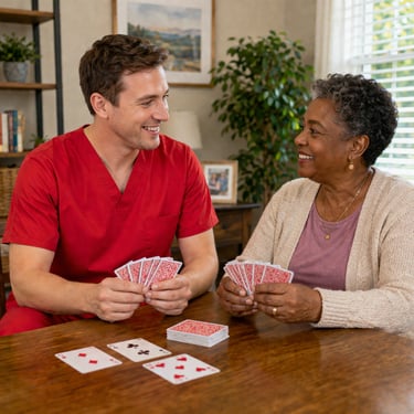 Male caregiver in red scrubs playing cards with a senior woman at a table, both smiling and enjoying time together