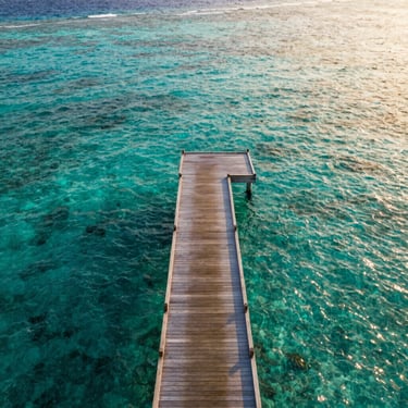 An aerial view of a private wooden dock leading into crystal clear turquoise waters of the Maldives, warm golden hour sun