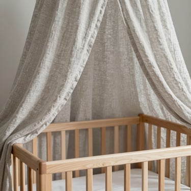 A delicate light gray linen canopy hanging over a clean wooden crib, soft shadows