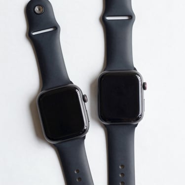 Overhead flat-lay of a smartwatch face-up on a clean white surface, neutral studio lighting, screen off, band flat beside it, no hands