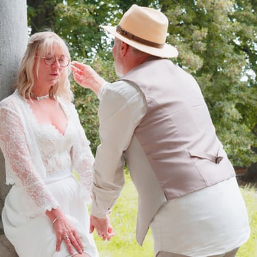 Un marié coiffé d'un chapeau de paille ajuste la coiffure de sa femme lors d'une séance photo de mariage en extérieur