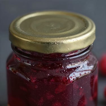 Macro shot of artisanal raspberry jam in an elegant glass jar, glinting gold lid, rich deep red texture, moody side-lighting, 50mm