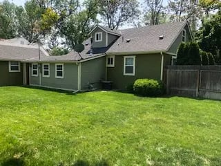 Green backyard of a student house near Boise State with olive siding, white windows, a large lawn, and a wood fence.