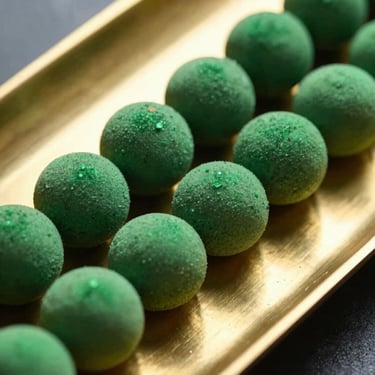 Extreme close-up of vibrant green herbal spheres arranged in a perfect diagonal line on a polished brass tray.