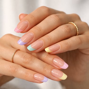 Hand with colorful pastel French tip manicure and gold rings, perfect for spring nail art inspiration.